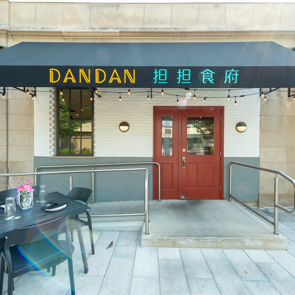 Dandan restaurant exterior with a black awning, red doors, and outdoor dining tables.