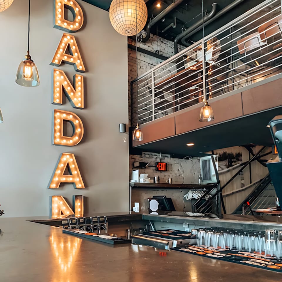 Modern restaurant interior featuring a bar, a large lighted "DANDAN" sign, and an upper seating area.